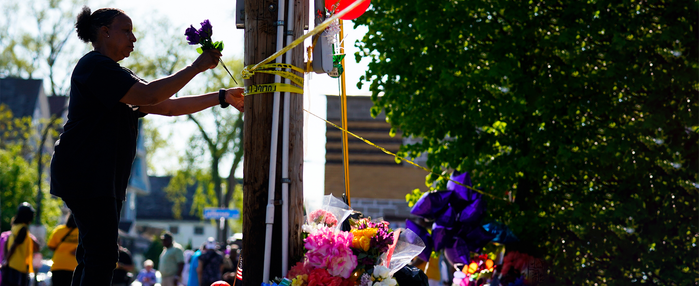 A woman in a blue shirt places flowers on a telephone pole serving as a makeshift memorial on May 15 outside the TOPS grocery store in Buffalo, NY, where 13 people were shot, 10 fatally on May 14, 2022. Photo credit: AP Photo/Matt Rourke.