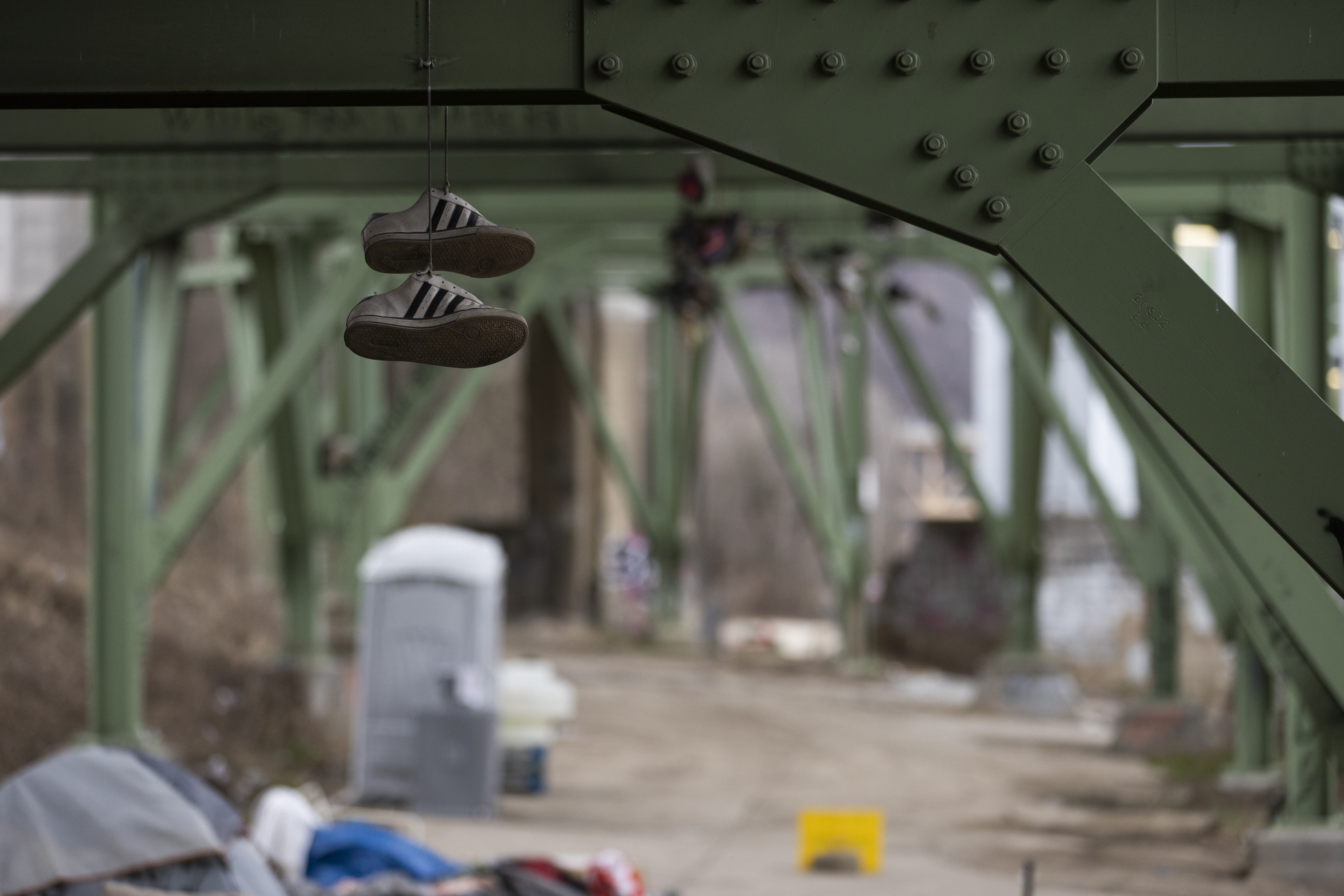 A pair of athletic shoes hang off of a bridge by the laces and personal items are scattered underneath