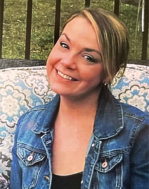 Smiling woman wearing a jeans jacket sitting outside. 