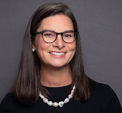 Woman with dark, straight hair wearing glasses and smiling to camera. 