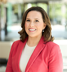 Woman with shoulder-length brown hair, wearing a white shirt and red blazer. 
