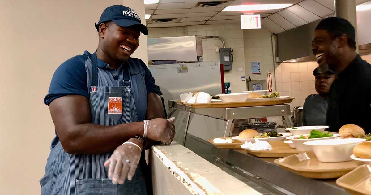 Kelvim Beachum, dressed in a blue t-shirt, talks with volunteers as they serve in a community food bank. (Photo by Kristin Kimball.)