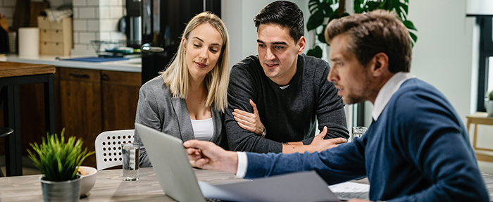 Young couple sitting at table looking at laptop with financial advisor.