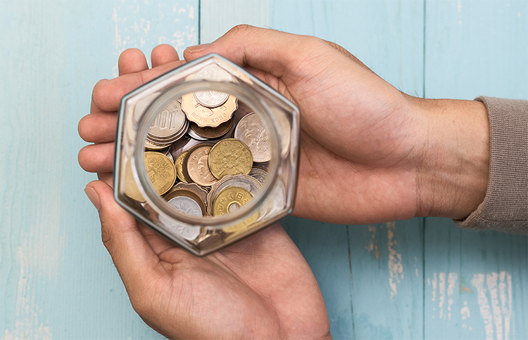 two hands holding a jar filled with coins