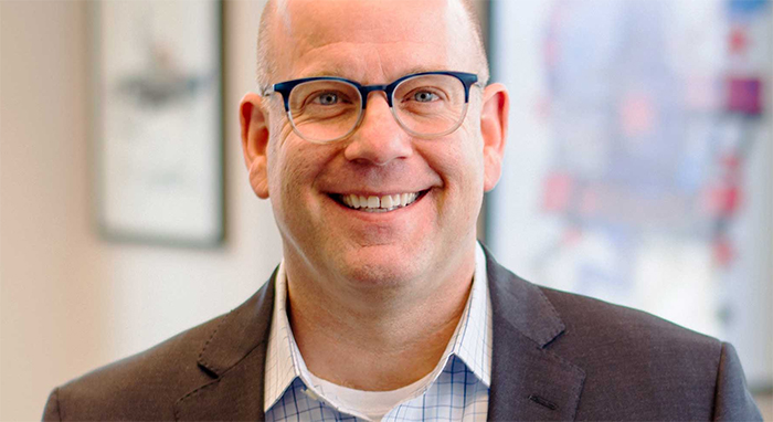 Man smiling at camera wearing glasses and a dark colored sport coat.